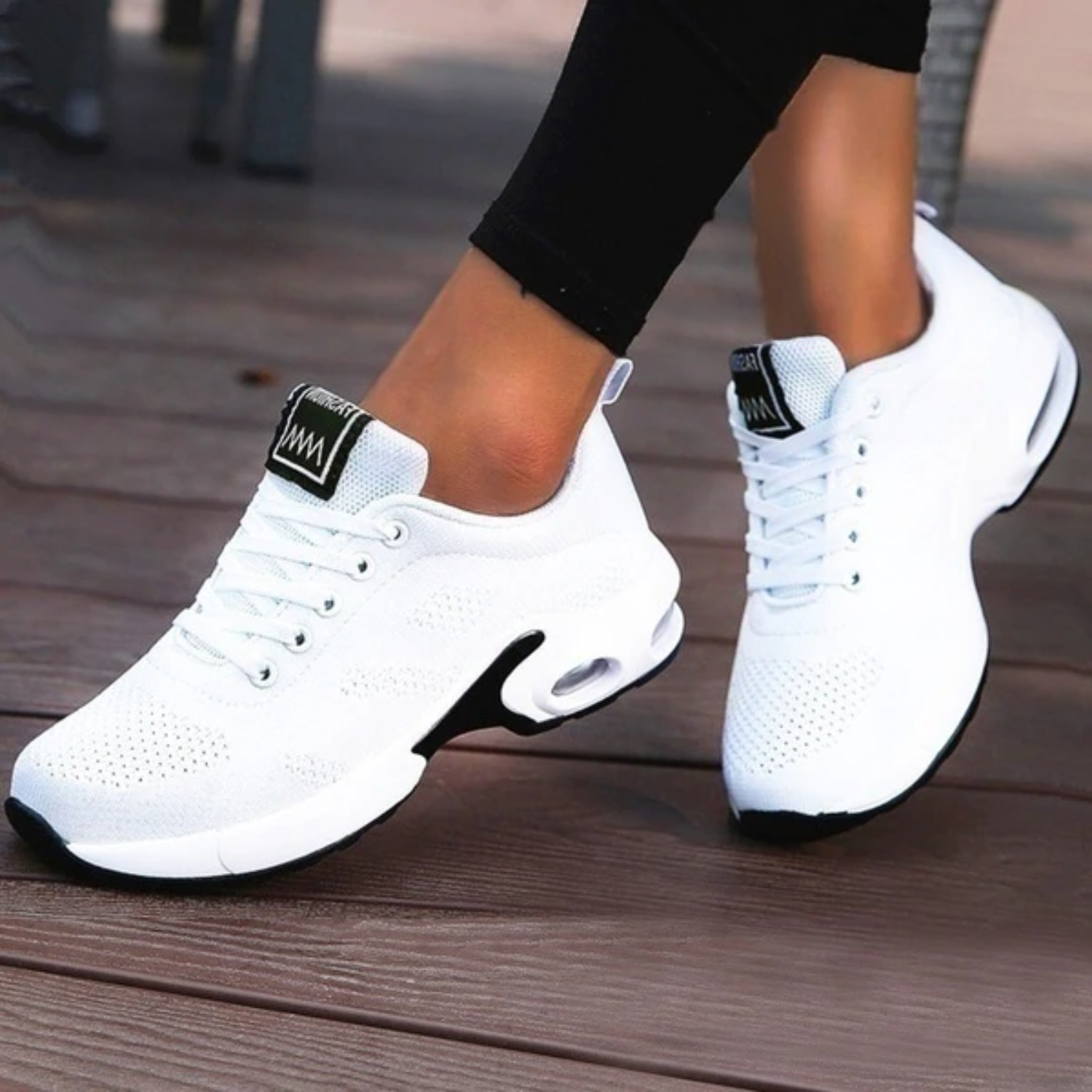 A pair of women's black orthopedic running shoes with white accents, designed for comfort and support, displayed on a wooden floor.